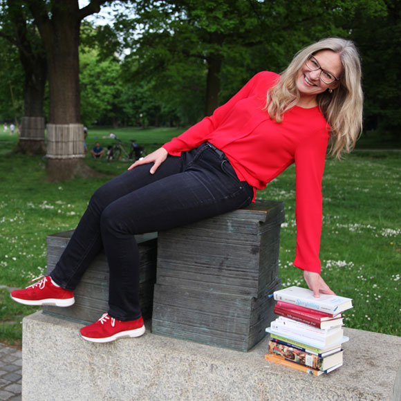 Susanne greift lachend zu ihrem Stapel Bücher neben sich auf dem Boden - Funfacts eben